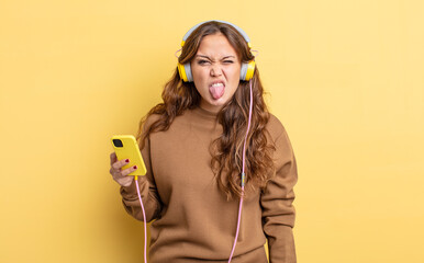 Wall Mural - hispanic pretty woman feeling disgusted and irritated and tongue out. headphones and smartphone concept