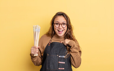 Wall Mural - hispanic pretty woman feeling happy and pointing to self with an excited. artist with brushes concept