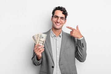 Wall Mural - hispanic handsome man smiling confidently pointing to own broad smile. business and dollar banknotes concept