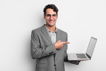 Wall Mural - hispanic handsome man smiling cheerfully, feeling happy and pointing to the side. business and laptop concept