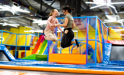 pretty girls jumping together on colorful trampoline at playground park. two sisters having fun duri