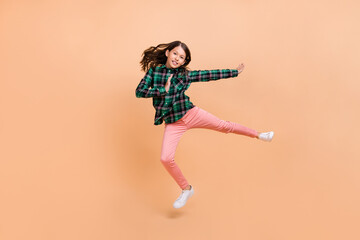 Photo of funky strong school girl dressed checkered clothes jumping high practicing karate isolated beige color background