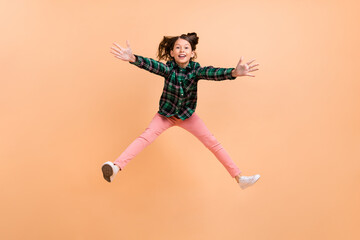 Poster - Photo of funny excited schoolgirl wear plaid outfit jumping high hands legs sides smiling isolated beige color background