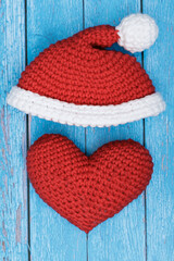 Sticker - knitted red heart with santa claus hat lies on a blue wooden background