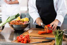 Cropped View Of Chef Cutting Bell Pepper Near Knifes And Vegetables In Kitchen