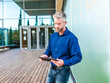 © ADDICTIVE STOCK - Serious man using tablet at entrance of modern office building