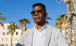 © ADDICTIVE STOCK - Serious black man in formal wear standing among palms