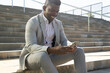 © ADDICTIVE STOCK - Smiling black businessman using smartphone on concrete steps
