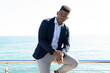 © ADDICTIVE STOCK - Well dressed black entrepreneur sitting on railing on seafront