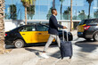 © ADDICTIVE STOCK - Black businessman with suitcase walking on sidewalk past taxi cars