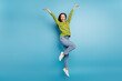 Photo of amazed funny lady jump raise arms wear green shirt jeans footwear isolated blue color background