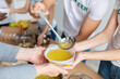 © Prostock-studio - Volunteers serving hot soup for homeless in community charity donation center, group of young people helping with food