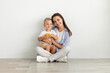 © Prostock-studio - Motherhood Concept. Beautiful Young Woman Sitting On Floor With Cute Infant Son