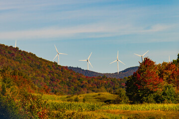 wind turbines along ridge line above  forest in autumn colors and field of golden corn ready for harvest 
