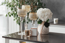 Three Glass Candlesticks On High Legs Stand On The Table Next To A Vase With Flowers And A Gold Candle In The Interior