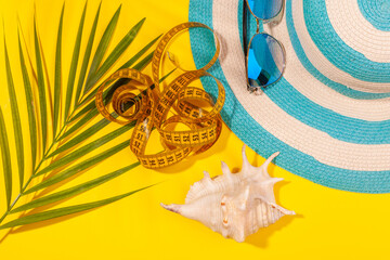 Wall Mural - Top view on striped hat, sunglasses and measuring tape with a seashell and a palm branch on a bright yellow background. Concept of slimming for a vacation at sea. Advertising space