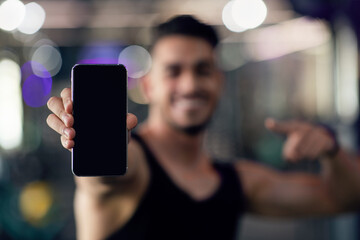 Wall Mural - Sports App. Happy young arab man holding and pointing at blank smartphone