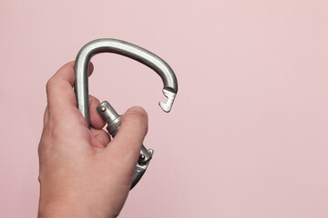 Carabiner for work at height. Climbing equipment on a pink background, carabiner in hand