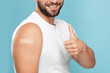 Smiling adult caucasian man with band aid on hand after injection show thumb up isolated on blue background