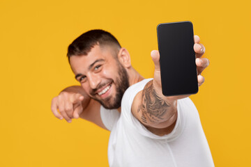 Cheerful emotional adult attractive caucasian male showing finger at smartphone with empty screen