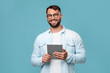 © Prostock-studio - Cheerful mature caucasian guy in glasses with tablet look at camera, isolated on blue background, free space