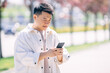© Ivan - Young asian man walks and uses smartphone on the street