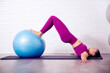 profesora de yoga y pilates mujer joven hace posiciones y posturas en un gimnasio o estudio sobre una esterilla y con un balon grande hinchable para trabajar en gimnasio ejercicios practicos