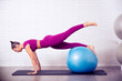 profesora de yoga y pilates mujer joven hace posiciones y posturas en un gimnasio o estudio sobre una esterilla y con un balon grande hinchable para trabajar en gimnasio ejercicios practicos