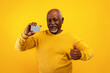 © Prostock-studio - Senior African American man holding credit card and showing thumb up on orange studio background