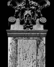 Photo Of An Acient Old Stone Column With Skull Sculpture And Decorative Elements On Dark Background.