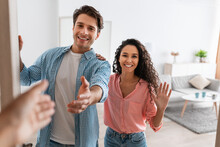 Happy Young Couple Inviting People To Enter Home, Shaking Hands
