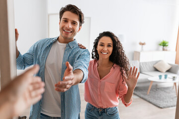 Happy young couple inviting people to enter home, shaking hands