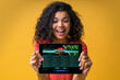 © wpadington - Portrait of cute happy girl with curly hair smiling and looking at the tablet with bookmaker application interface template and making funny face expression laughing with mouth open