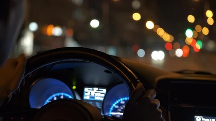 Canvas Print - Close up of driver hands holding steering wheel driving car with blurred city street lights on background at night