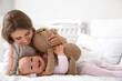 © Pixel-Shot - Young mother with her cute little baby and teddy bear on bed