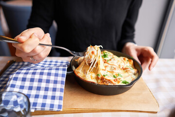 Wall Mural - Potato with cheese casserole in a cast-iron frying pan. Close-up of a woman eating with a fork. Latvian cuisine