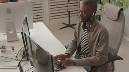 Medium slowmo shot of young African-American man working on PC at modern programmers office