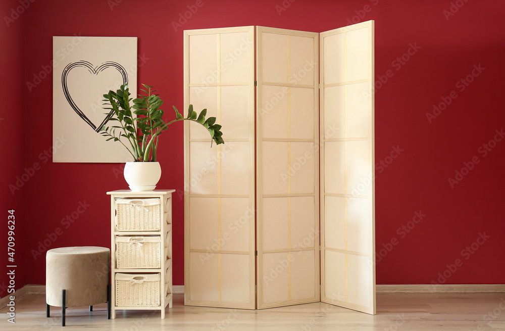 Stylish folding screen and pouf near red wall