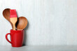 Set of wooden kitchen utensils in red cup on light grey table. Space for text