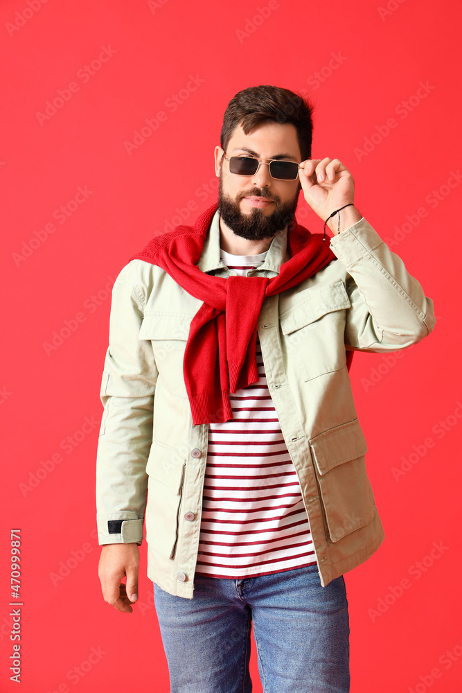 Handsome man in stylish sunglasses and jacket on red background