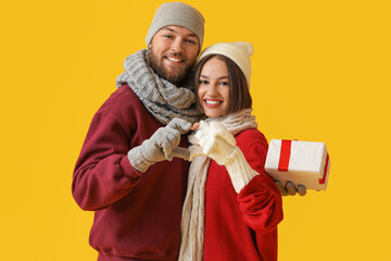 Wall Mural - Happy young couple in stylish winter clothes and with Christmas gift on color background
