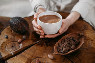 hot handmade ceremonial cacao in white cup. woman hands holding craft cocoa, top view on wooden tabl