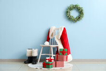 Chair With Santa Claus Costume, Boots And Christmas Gifts Near Color Wall