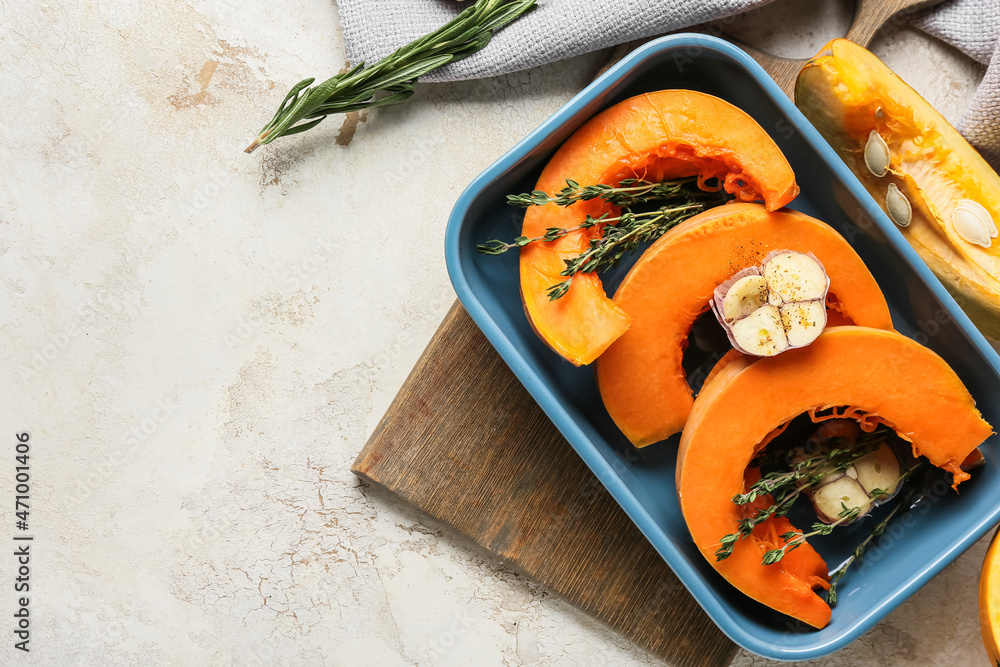 Baking dish with fresh pumpkin pieces on light background
