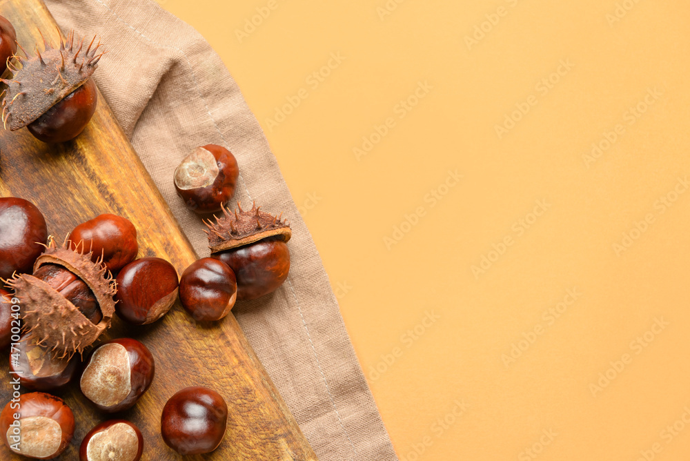 Wooden board with chestnuts on color background, closeup