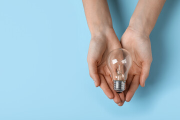 Wall Mural - Woman holding light bulb on color background, top view. Space for text