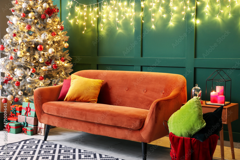 Red sofa with Christmas tree, gifts and glowing lights near green wall