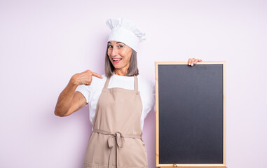 Wall Mural - senior pretty woman feeling happy and pointing to self with an excited. chef and blackboard concept
