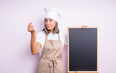 Wall Mural - senior pretty woman making capice or money gesture, telling you to pay. chef and blackboard concept