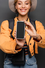 Smartphone With Blank Screen In Hands Of Blurred Cheerful Tourist On Grey